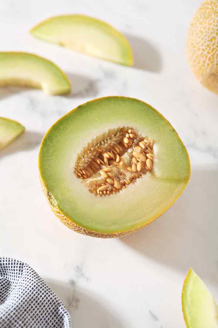 A halved Galia melon is shown on a marble backdrop