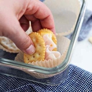 A woman picks up a cracker sandwich from a food storage container