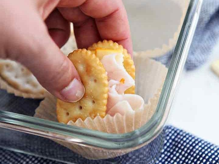 A woman picks up a cracker sandwich from a food storage container