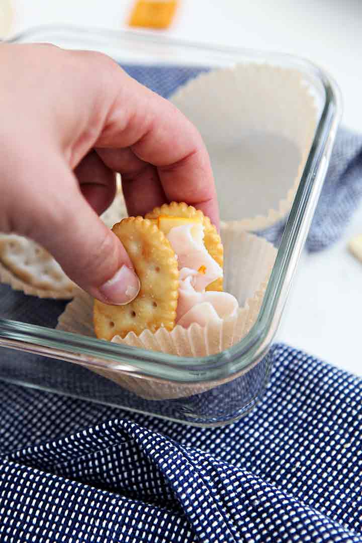 A woman picks up a cracker sandwich from a food storage container