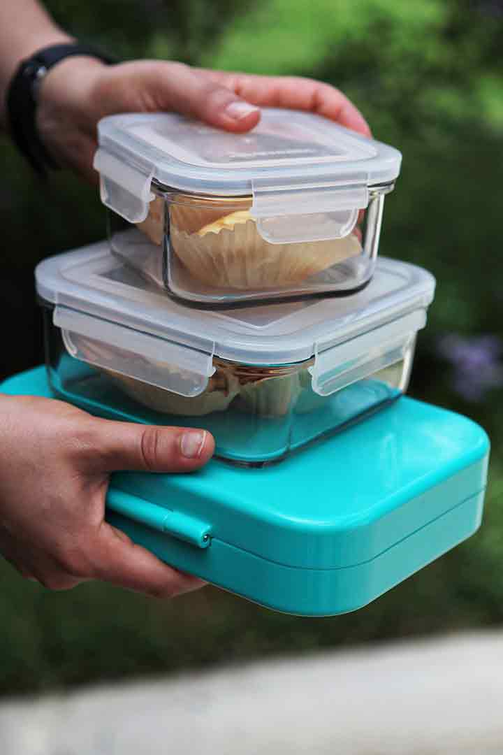 A man holds three food storage containers of cracker sandwiches to be taken to a picnic