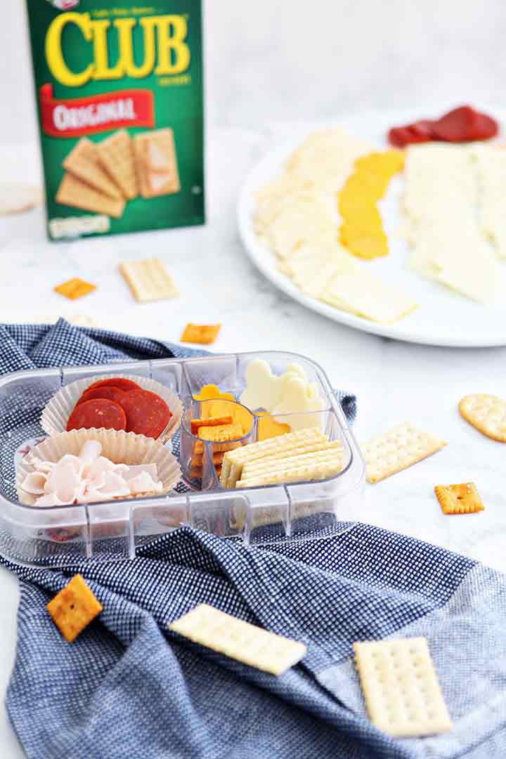 A make-your-own cracker snack kit is shown with several meats and cheese and a Club cracker box behind it