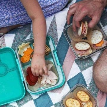 A girl and a man eat cracker sandwiches out of portable storage containers on a picnic