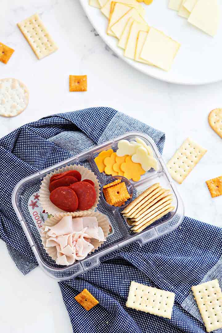 A make-your-own cracker snack kit is shown from above with several meats and cheese