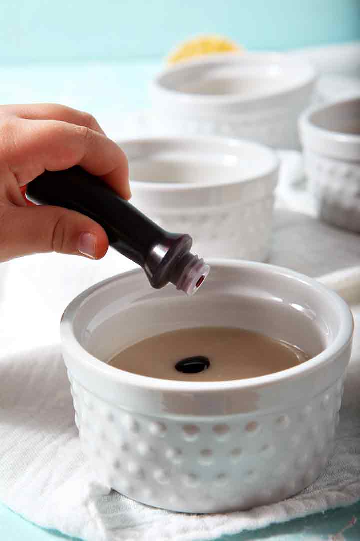 A girl drops food coloring into icing in a small white bowl