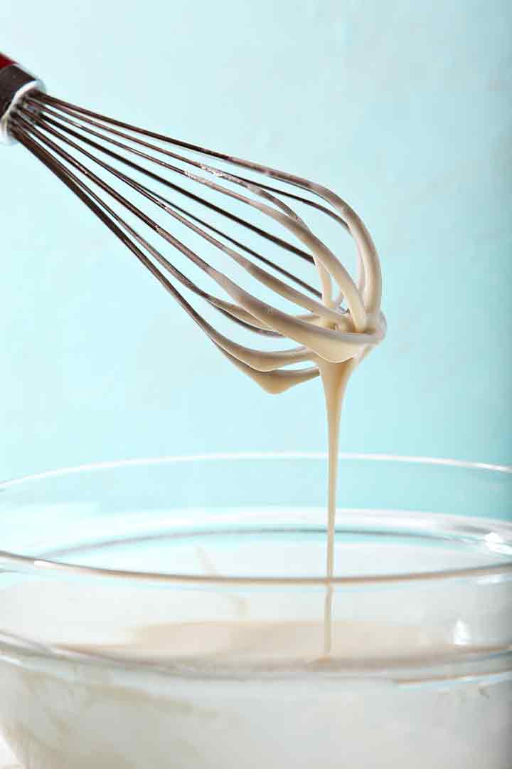 Icing is drizzled from a whisk into a bowl