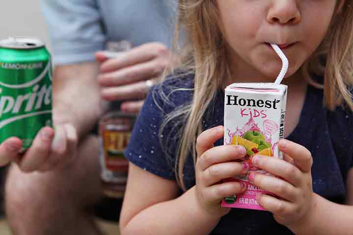 A girl drinks an Honest Kids juice box while a man sits behind her with a Sprite and a Gold Peak tea