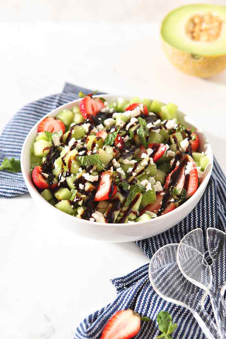 A Strawberry Melon Salad is shown in a bowl with tongs, ready for serving