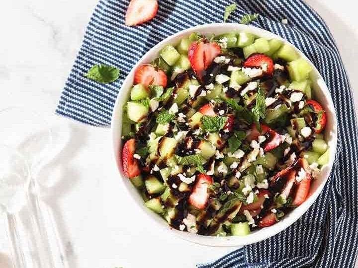 Overhead image of the final Strawberry Melon Salad in a white bowl with a blue napkin