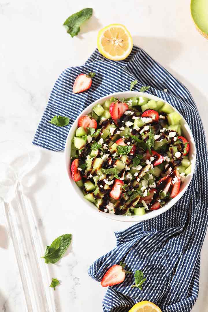 Overhead image of the final Strawberry Melon Salad in a white bowl with a blue napkin