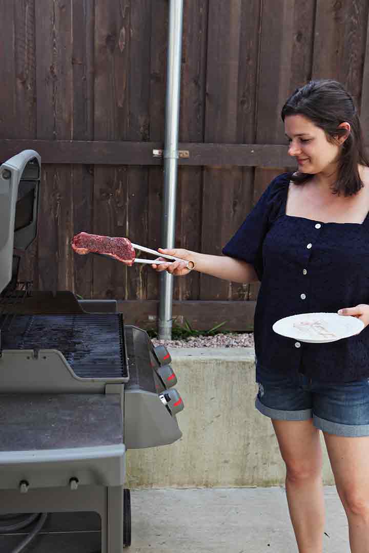 A woman places a New York Strip Loin Steak onto a sizzling hot grill