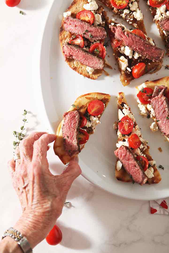 A woman picks up a piece of the Grilled Steak Flatbread Pizza, from above