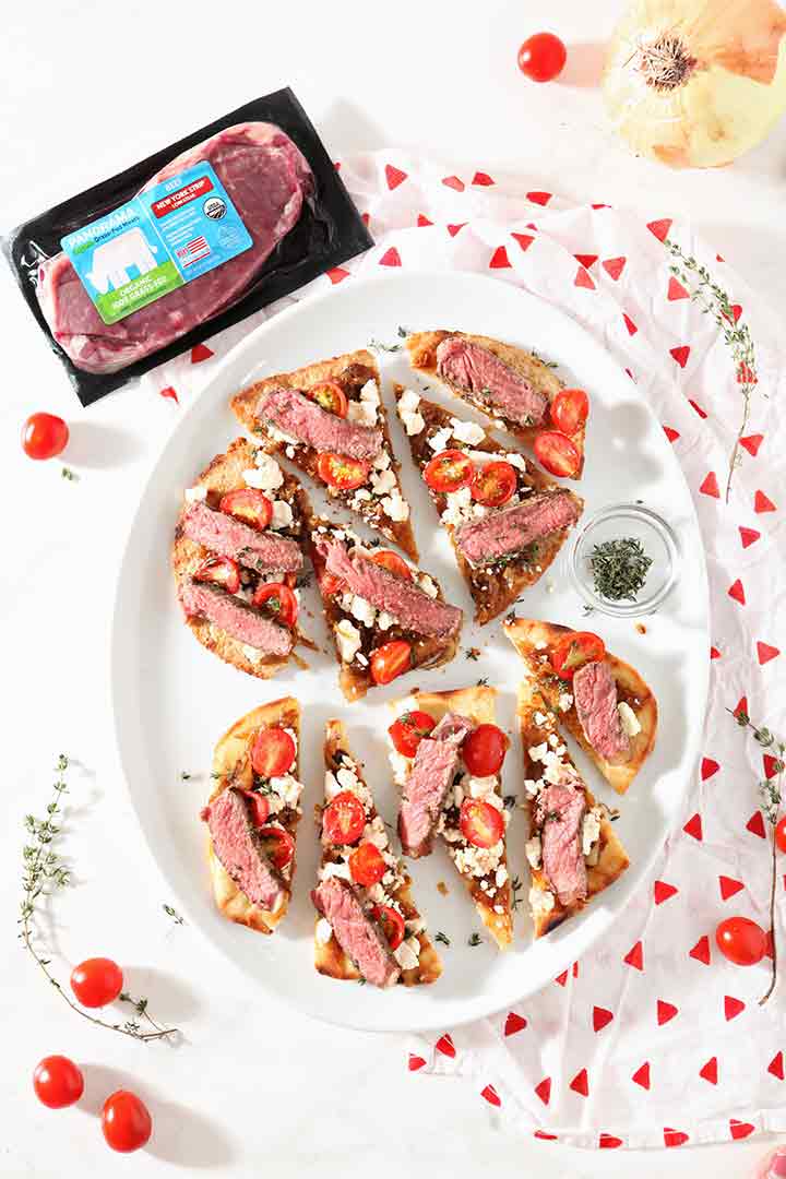 Two Grilled Steak Flatbread Pizzas are shown on a tablescape with a package of Panorama NY Strip Steak