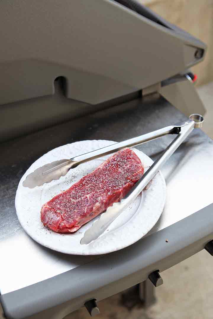 A New York strip loin steak is shown beside a grill, before cooking