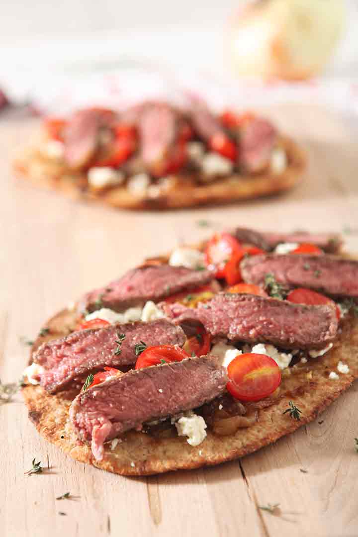 Close up of a grilled steak flatbread pizza recipe on a wooden cutting board