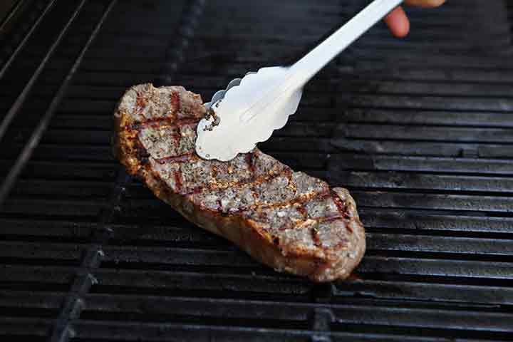 A woman flips a New York Strip Loin Steak on the grill