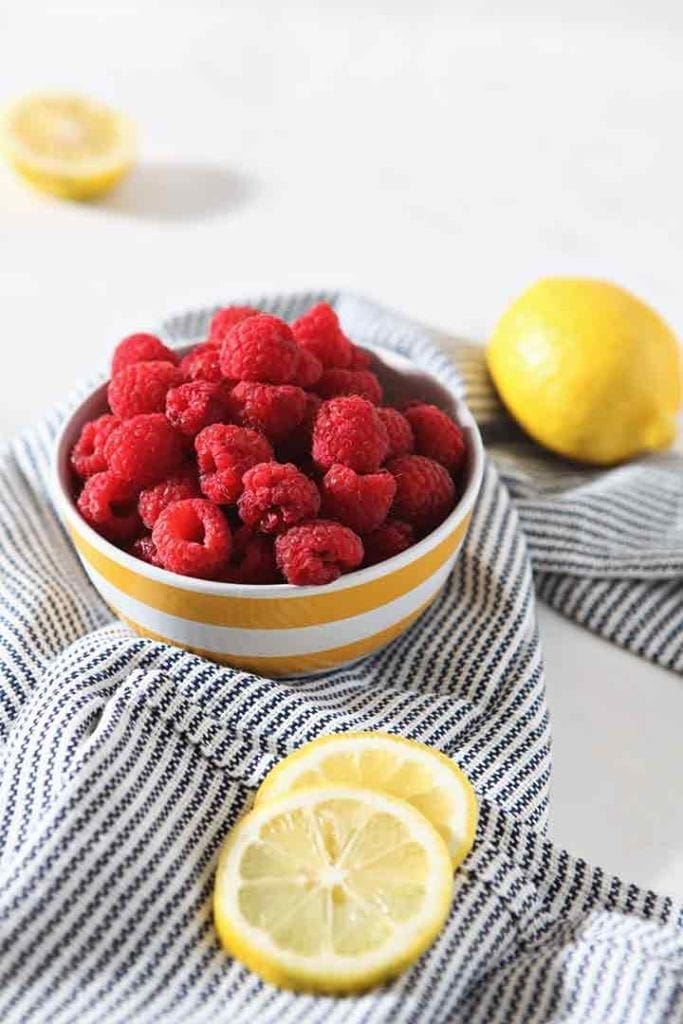 A bowl of raspberries with whole and sliced lemons