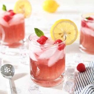 Three glasses of Vodka Lemonade with Raspberry are surrounded by ice and ingredients