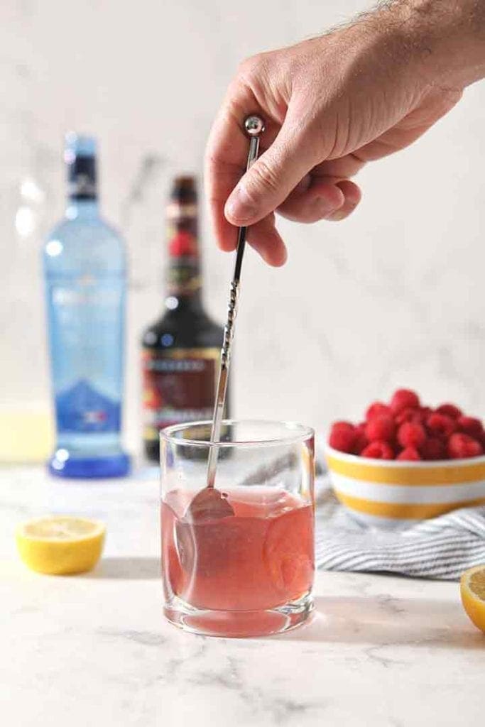 A man stirs a drink with a cocktail spoon