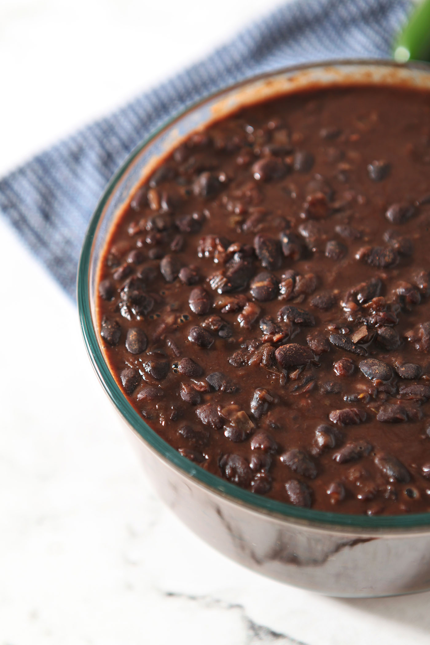 A Pyrex dish holding black bean dip after it has cooled on a marble surface next to a blue linen.