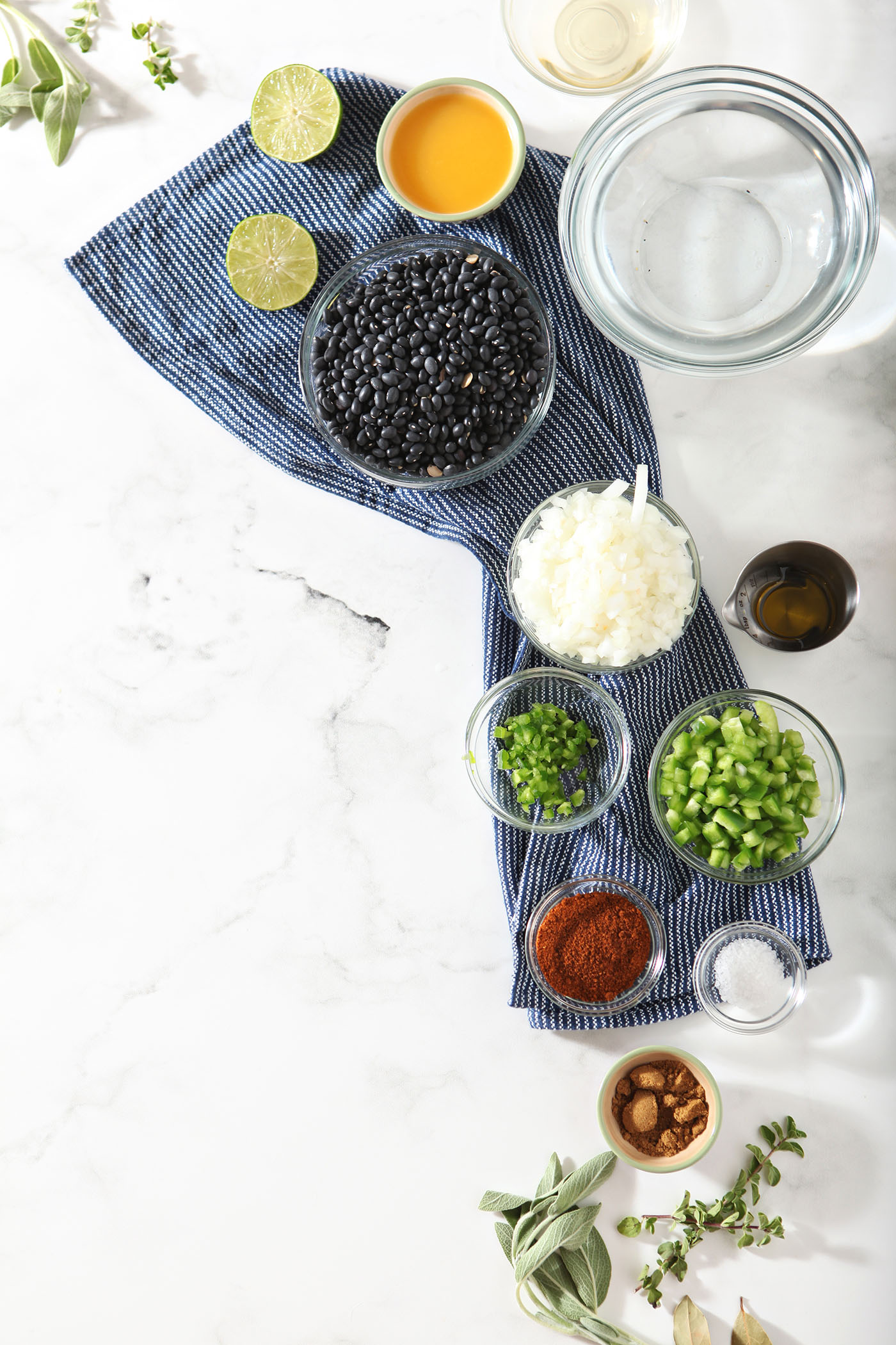 Bowls holding ingredients to make homemade black bean dip with dried black beans on a marble surface with a dark blue striped linen