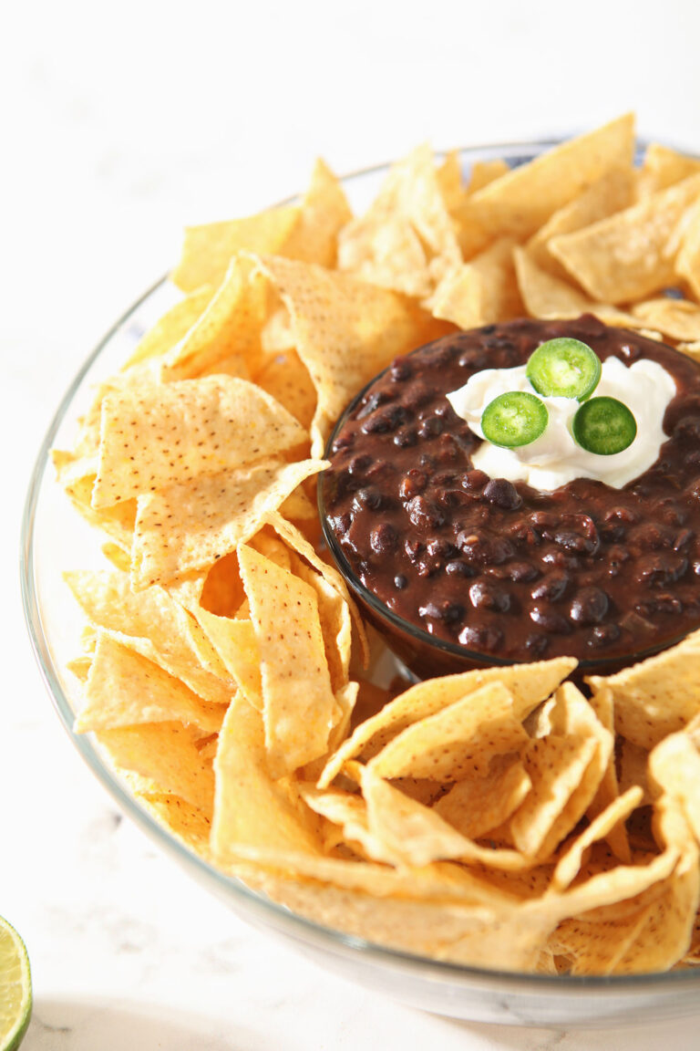 Chips surround a bowl of black bean dip, garnished with sour cream and jalapeno slices.