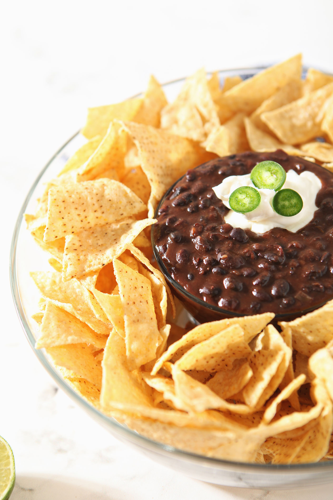 Chips surround a bowl of black bean dip, garnished with sour cream and jalapeno slices.