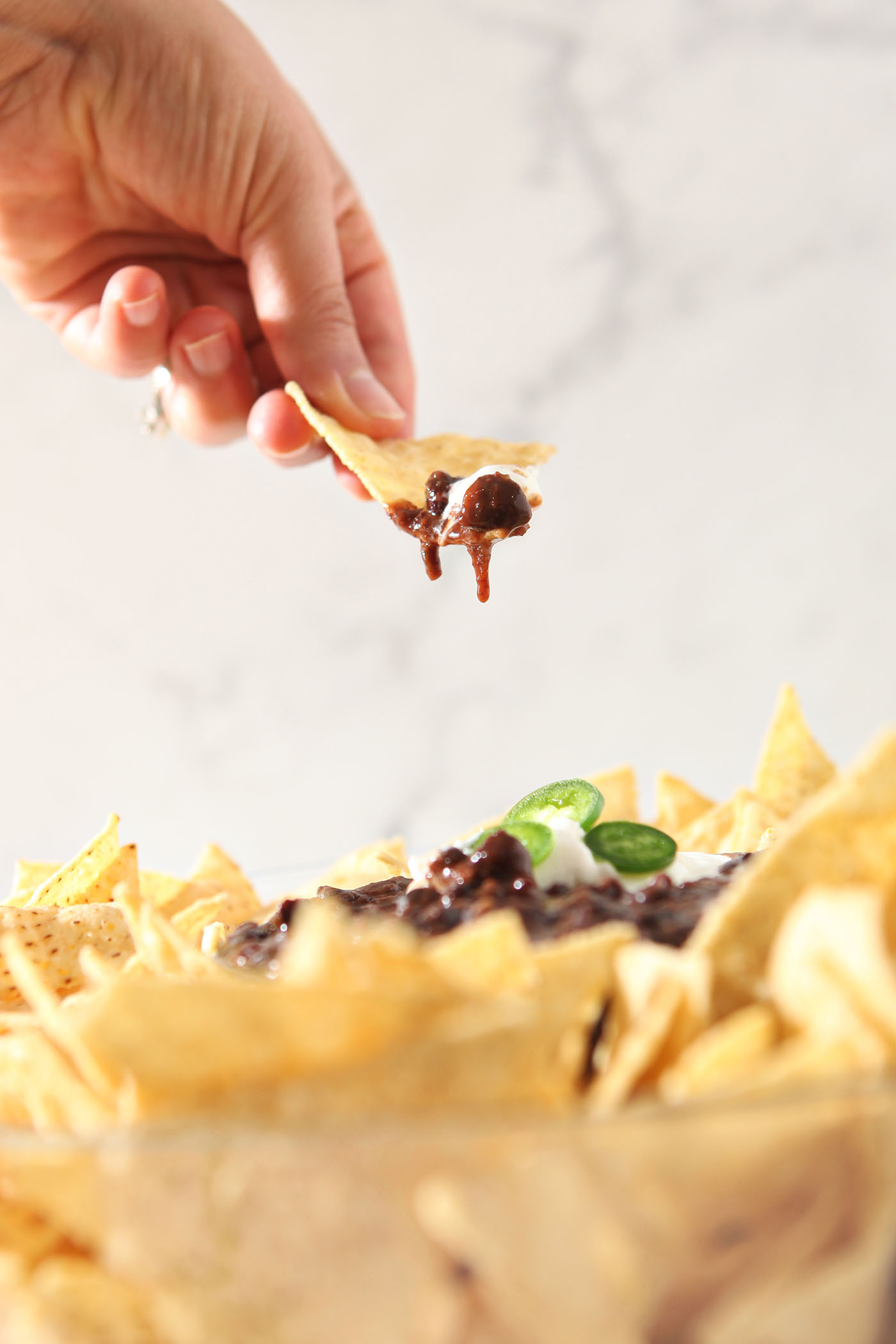 A tortilla chip lifts out of a bowl of black bean dip.