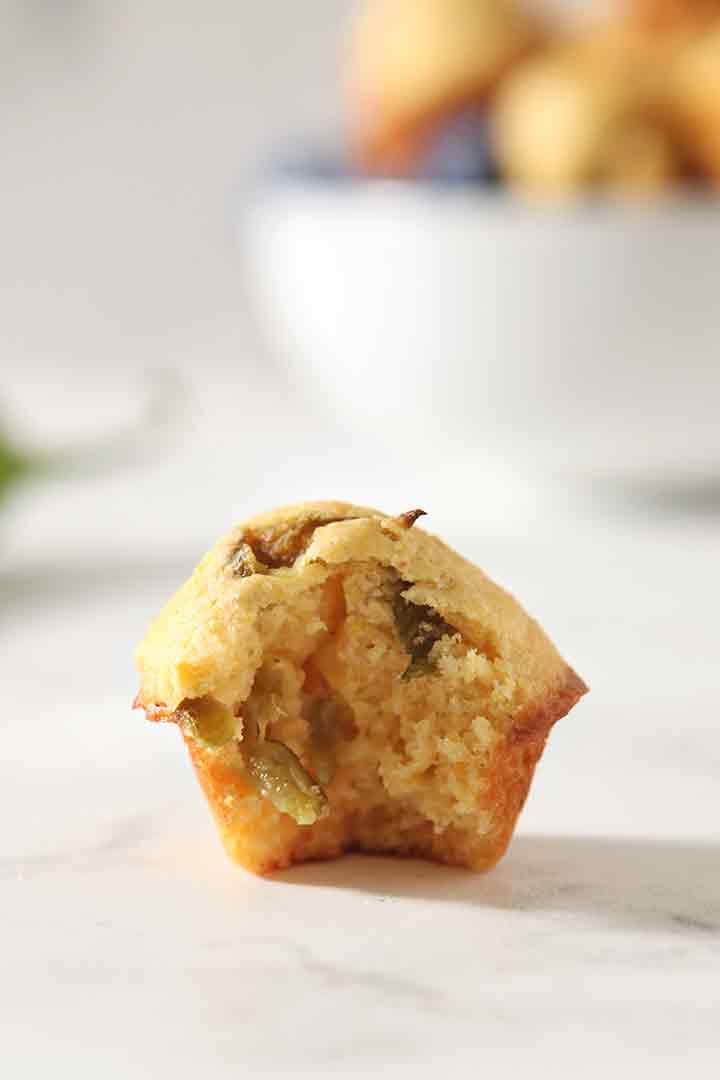 Close up of a bitten-into Hatch Chile Mini Cornbread Muffin on a marble surface