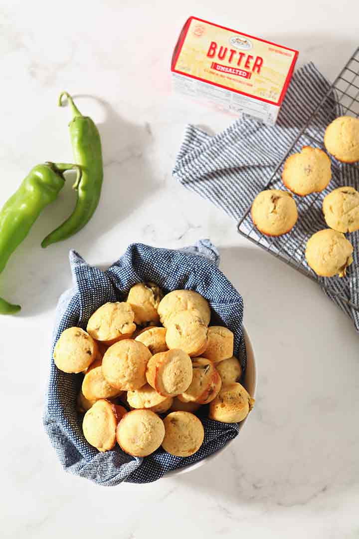 Muffins, shown from above, in a bowl and on a cooling rack, surrounded by Hatch chiles