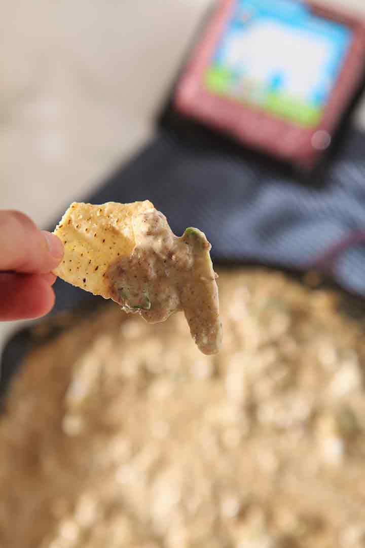 A tortilla chip holding dip is lifted upward out of the skillet