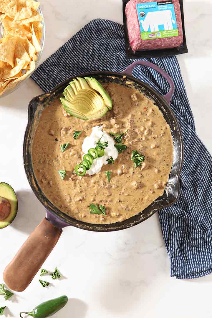 Overhead image of Homemade Loaded Queso in a skillet, garnished and surrounded by ingredients and chips