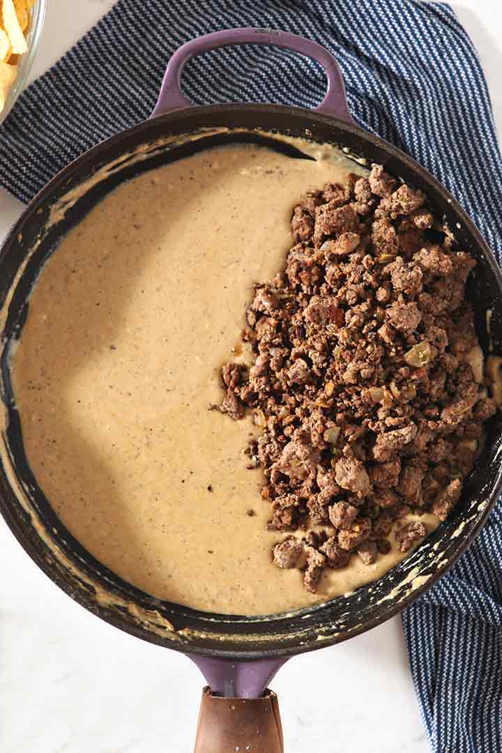 Close up of the queso in a skillet with the ground beef mixture on top of it before mixing