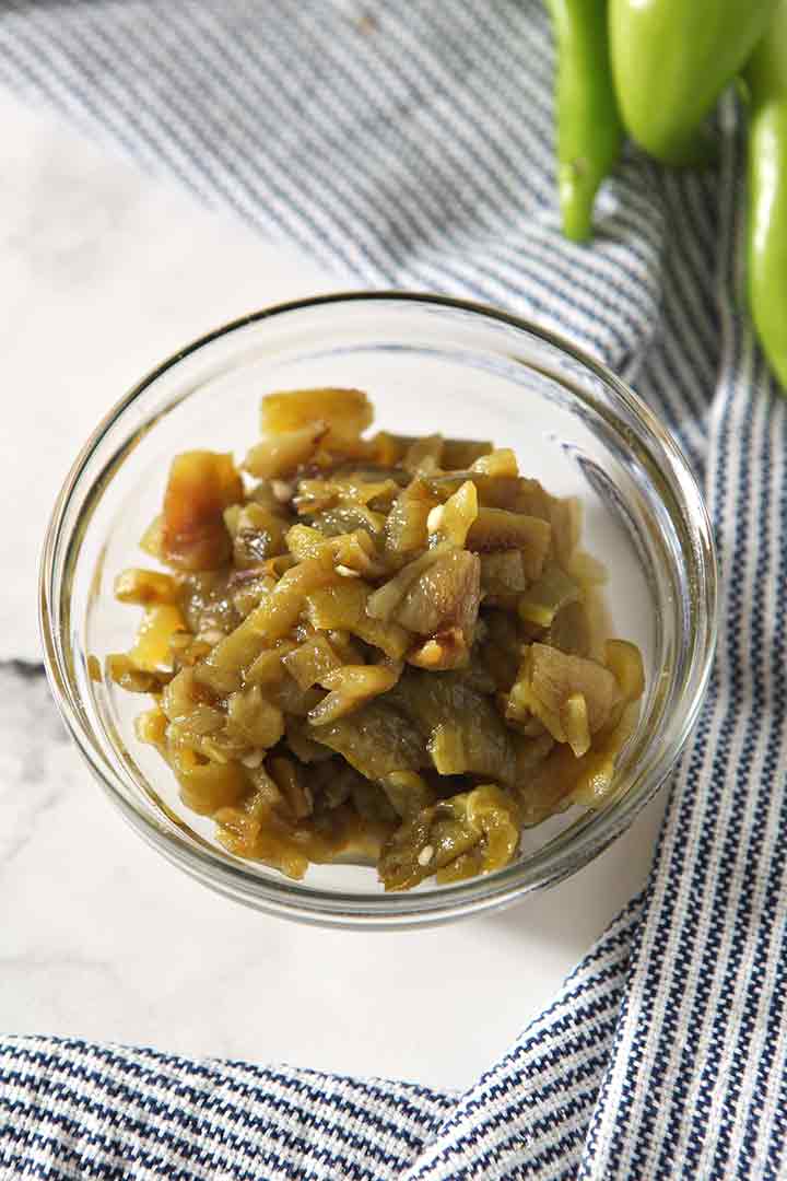 Chopped and roasted chiles are shown in a bowl, surrounded by fresh chiles