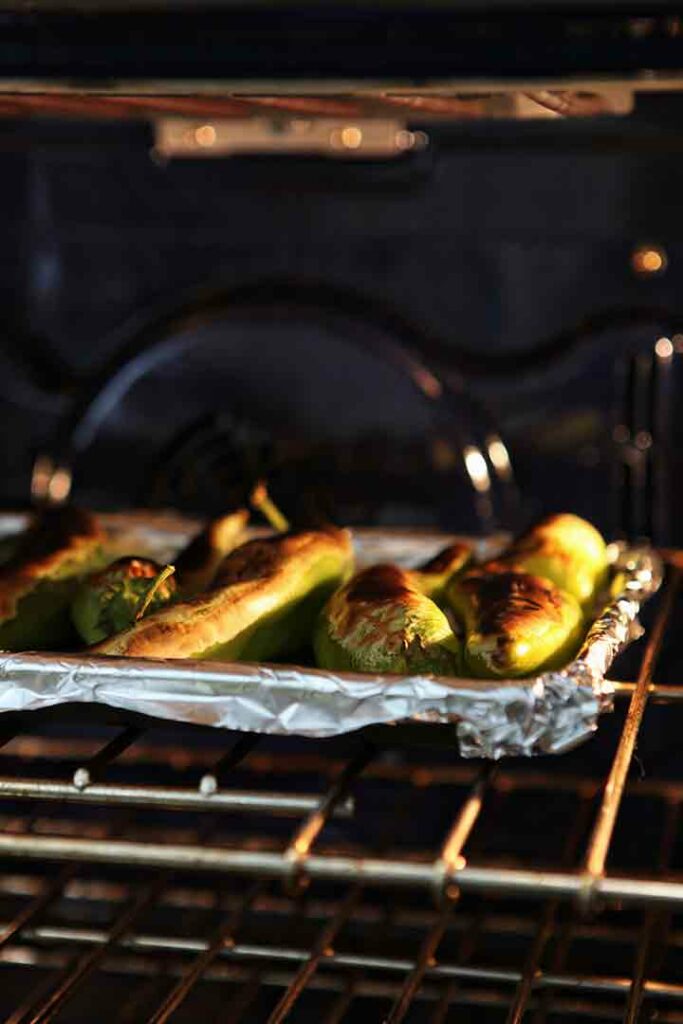 Blistered Hatch chiles on a baking sheet, under the broiler in the oven