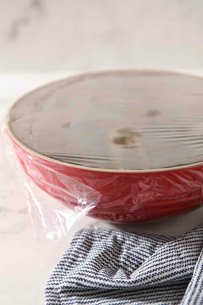 Roasted peppers steam under a plastic wrapped bowl