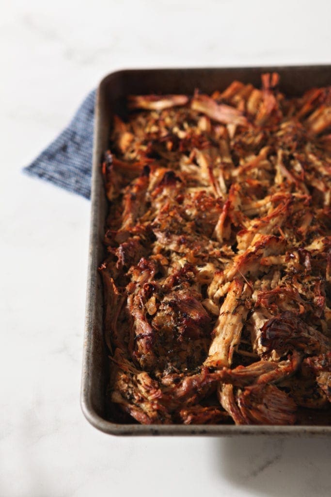 Shredded carnitas are shown on a baking sheet, after crisping up in the oven