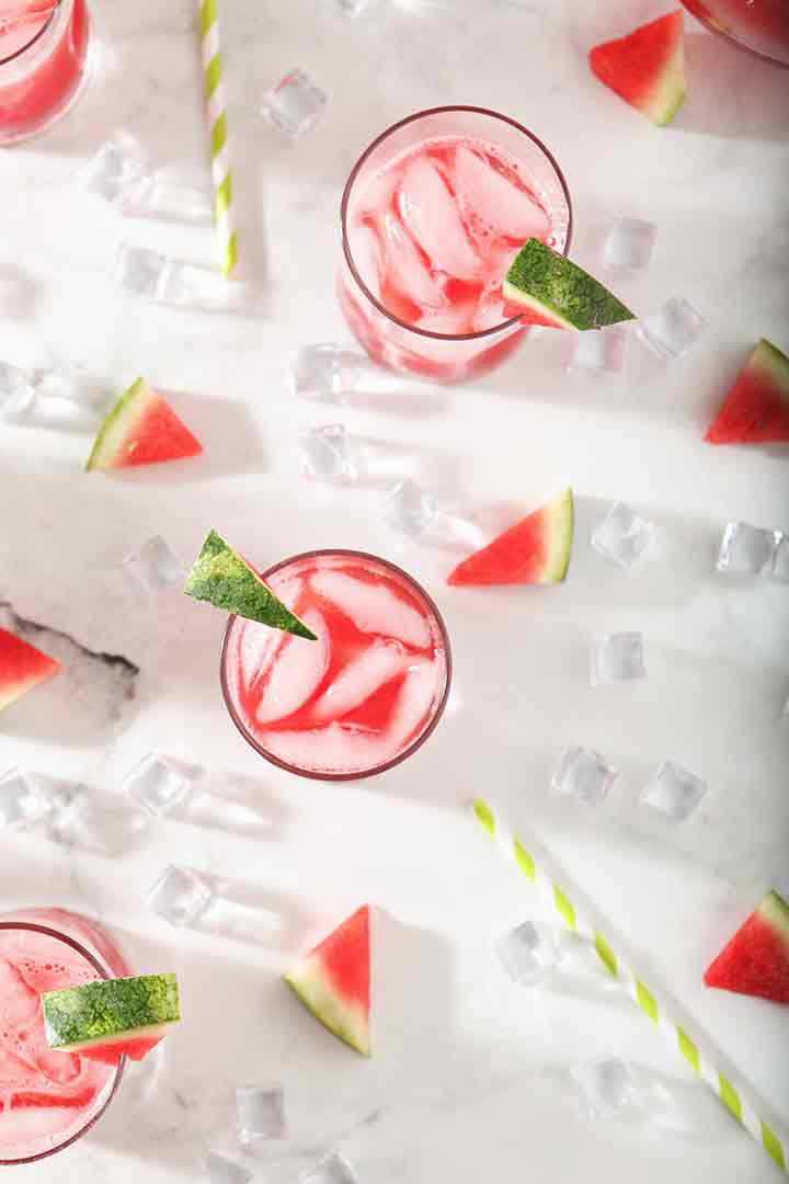 Several Watermelon Agua Frescas from above, surrounded by ice and watermelon wedges