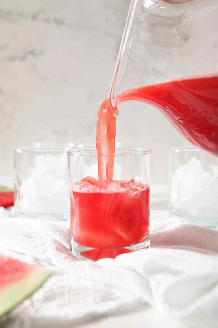 Watermelon Agua Fresca is poured into a glass, surrounded by other glasses