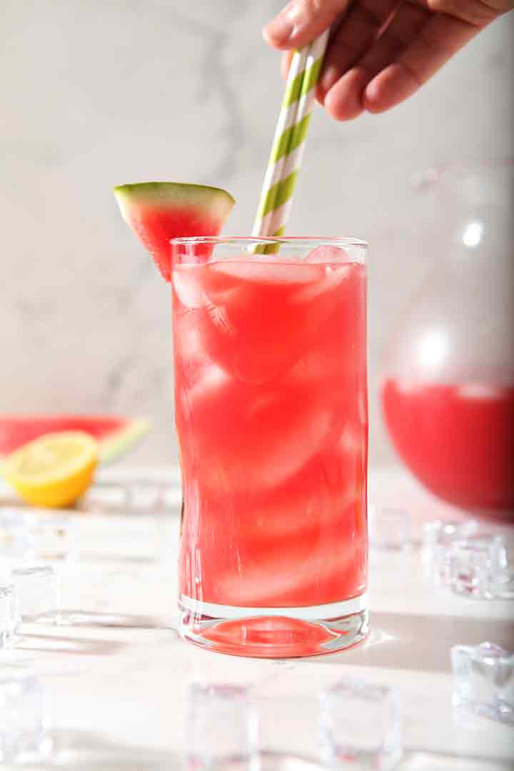 A woman places two colorful paper straws into a glass of Watermelon Agua Fresca