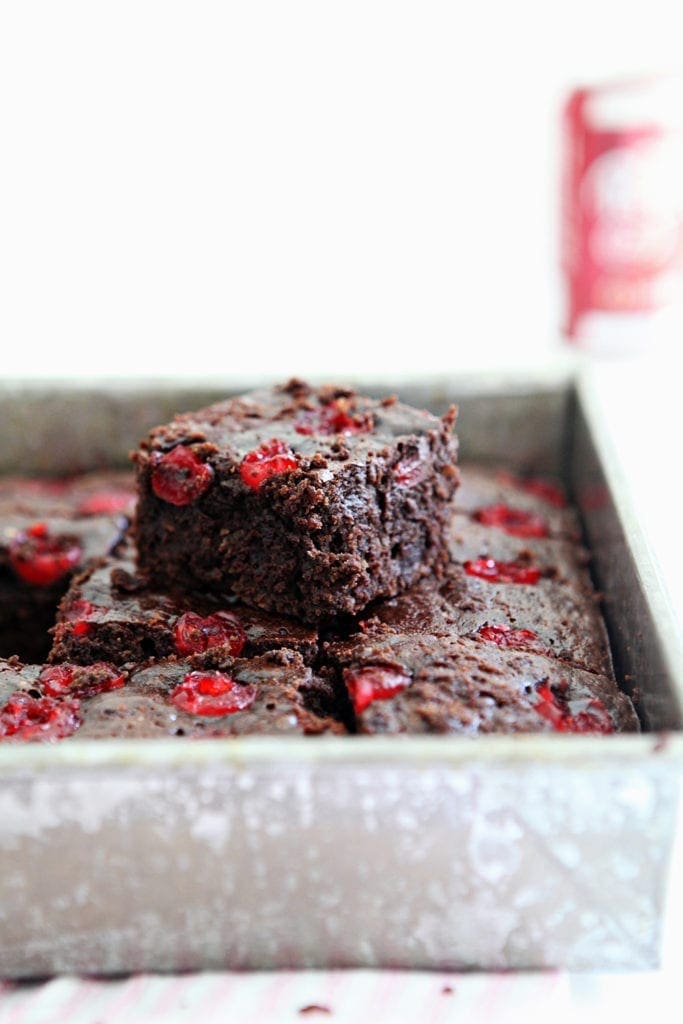 A Dr Pepper Chocolate Cherry Brownie sits on top of others in a pan, with Dr Pepper in the background