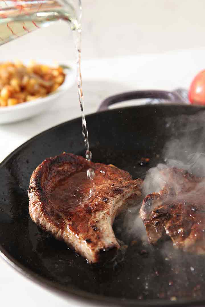 Wine (or stock) is poured on top of the pork chops to deglaze the pan