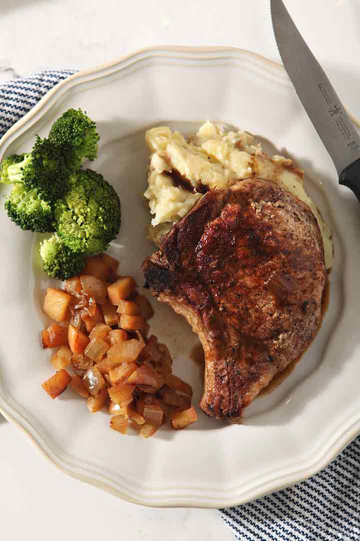 Close up of an Cinnamon Apple Pork Chop on a plate with steamed broccoli and mashed potatoes