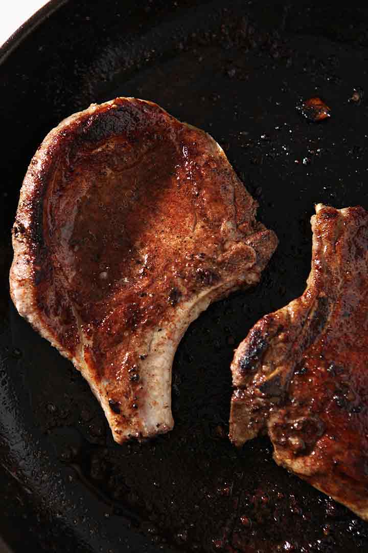 Pork chops sear in a pan, close up