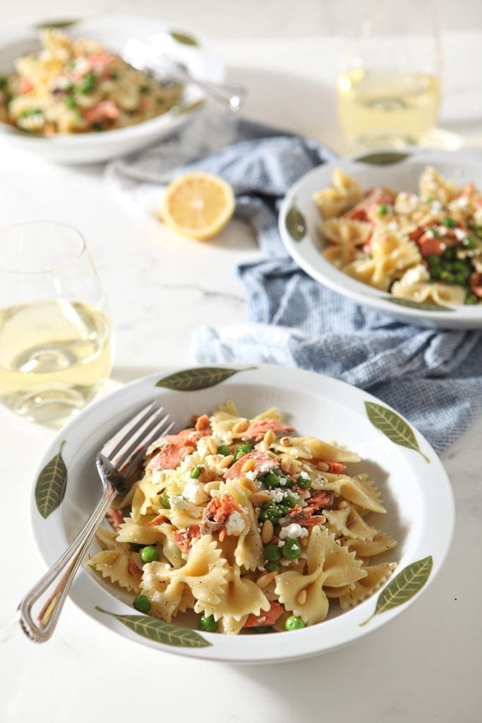 Three bowls of served Lemon Salmon Pasta are shown with wine, on a marble backdrop