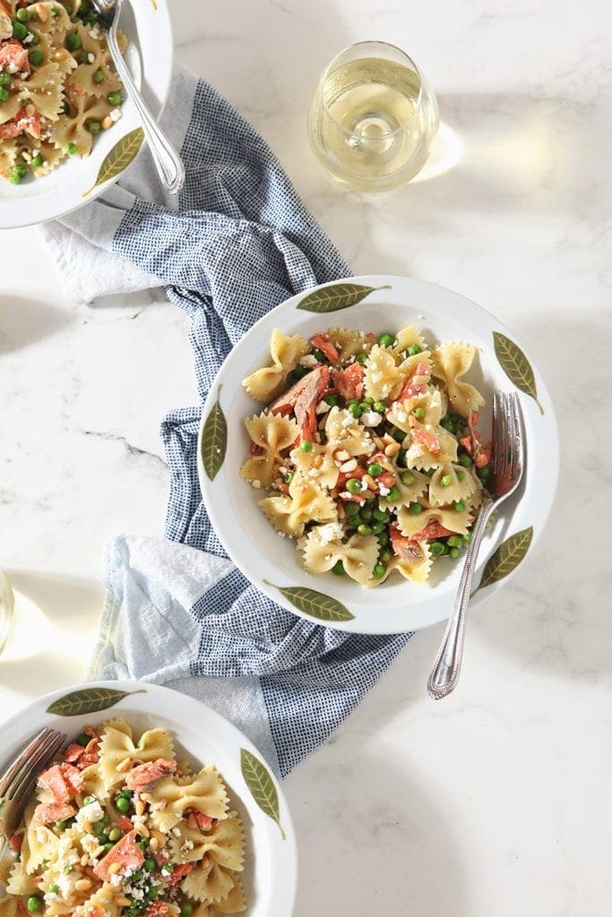 Three bowls holding Lemon Salmon Pasta are shown from above with wine