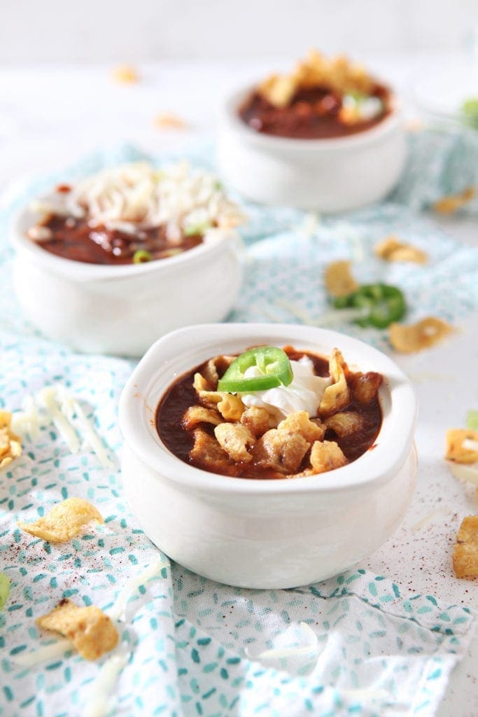 Three bowls of Homemade Texas Chili are topped with various ingredients