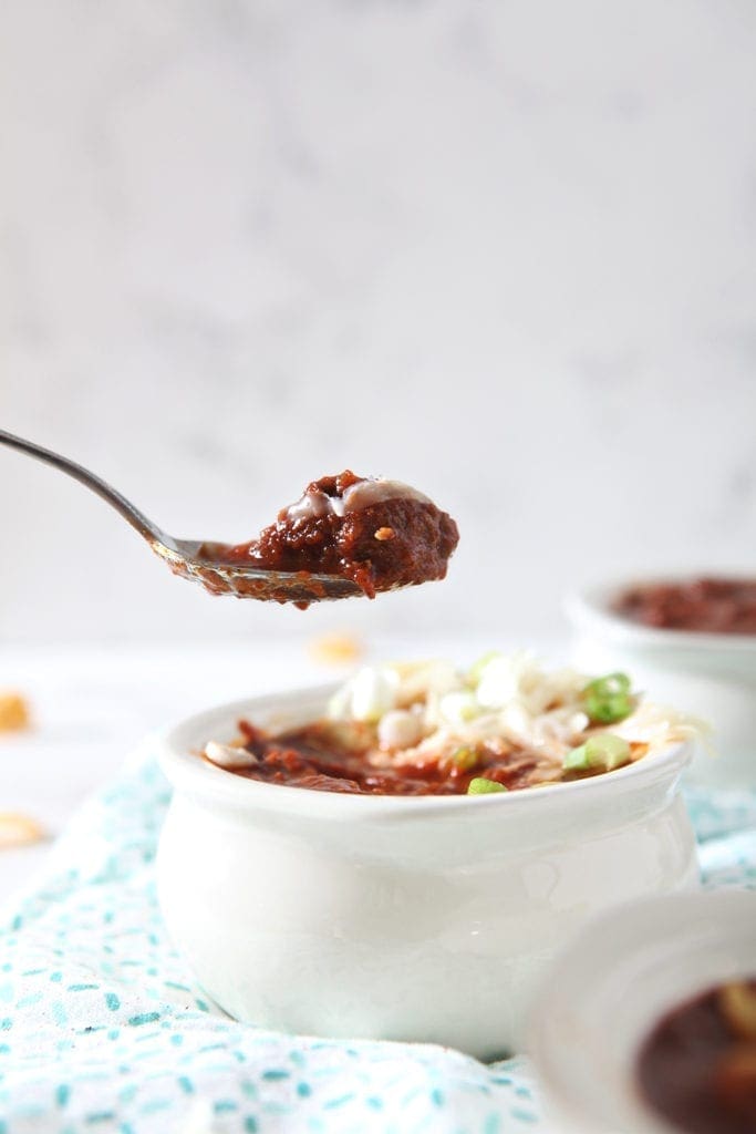 A spoon lifts a hunk of stew meat out of a bowl of chili