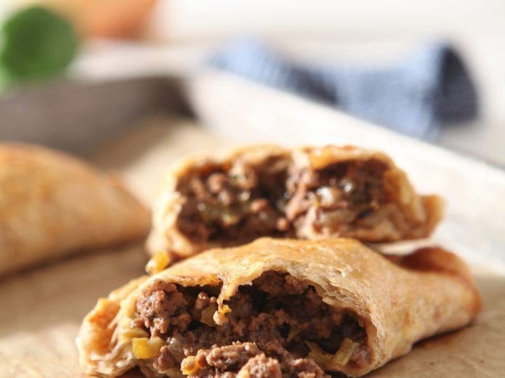 A halved meat pie is shown on a baking sheet, with ingredients in the background