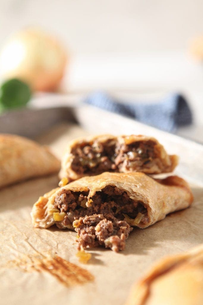 A halved meat pie is shown on a baking sheet, with ingredients in the background